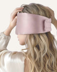 Person wearing a pink silky eye mask against a light background