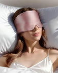 Woman wearing a pink sleep mask lying on white pillow.